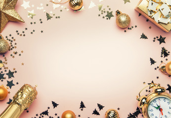 Christmas or New Year composition, frame, pink background with gold Christmas decorations, stars, snowflakes, balls, alarm clock, gift box and bottle of champagne, top view