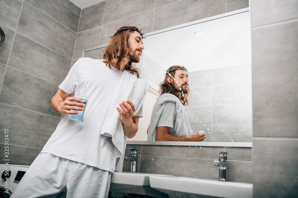 low angle view of Jesus in crown of thorns rinsing mouth by mouthwash liquid in bathroom low angle view of Jesus in crown of thorns rinsing mouth by mouthwash liquid in bathroom