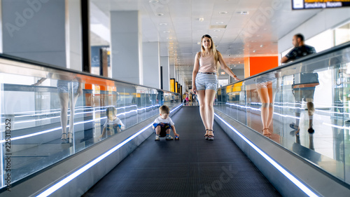 Beautiful young woman with toddler son standing on moving walkway at airport terminal