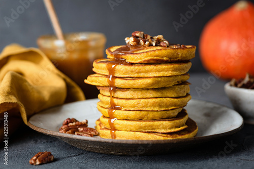 Pumpkin pancakes with caramel sauce and pecan nuts, black concrete background. Closeup view, selective focus
