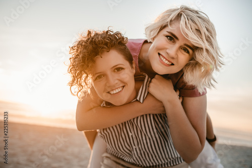 Young woman giving her girlfriend a piggyback at the beach