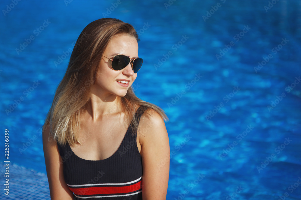 Woman wearing sunglasses with long beautiful legs and hair sits on the edge of a pool with blue water. Woman wearing sunglasses with long beautiful legs and hair sits on the edge of a pool with blue water.