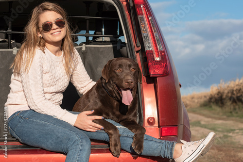 A beautiful young blond-haired woman is having fun with her big brown labrador dog in car