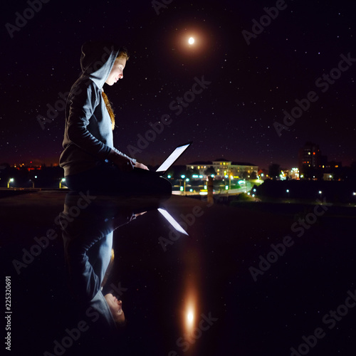Young white redhead skinny girl  weared in grey hoody  sitting outdoors and working with laptop in night