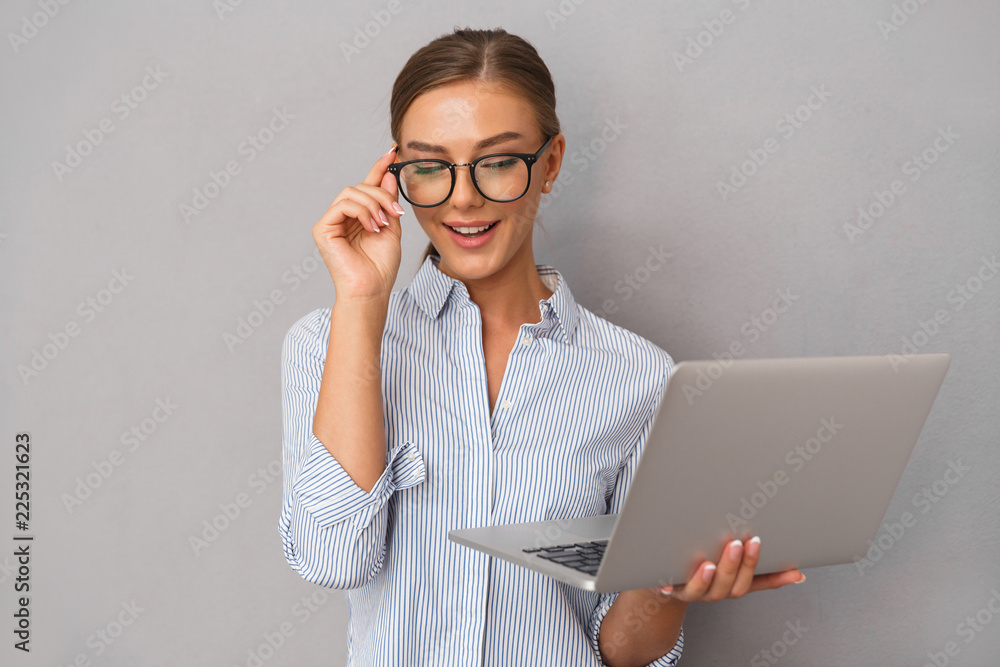 Business young woman posing isolated over grey wall background using laptop computer. Business young woman posing isolated over grey wall background using laptop computer.