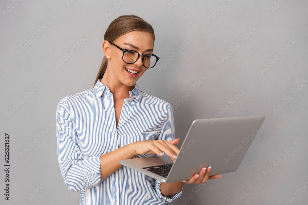 Business young woman posing isolated over grey wall background using laptop computer.