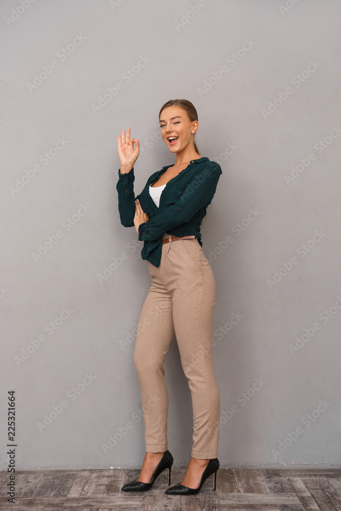 Beautiful business woman posing isolated over grey wall background showing okay gesture.