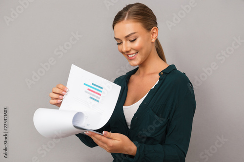 Woman posing isolated over grey wall background holding clipboard with graphics.