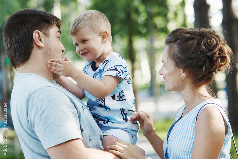 Fototapeta premium Young happy family: father, mother and blond boy walking in the park.
