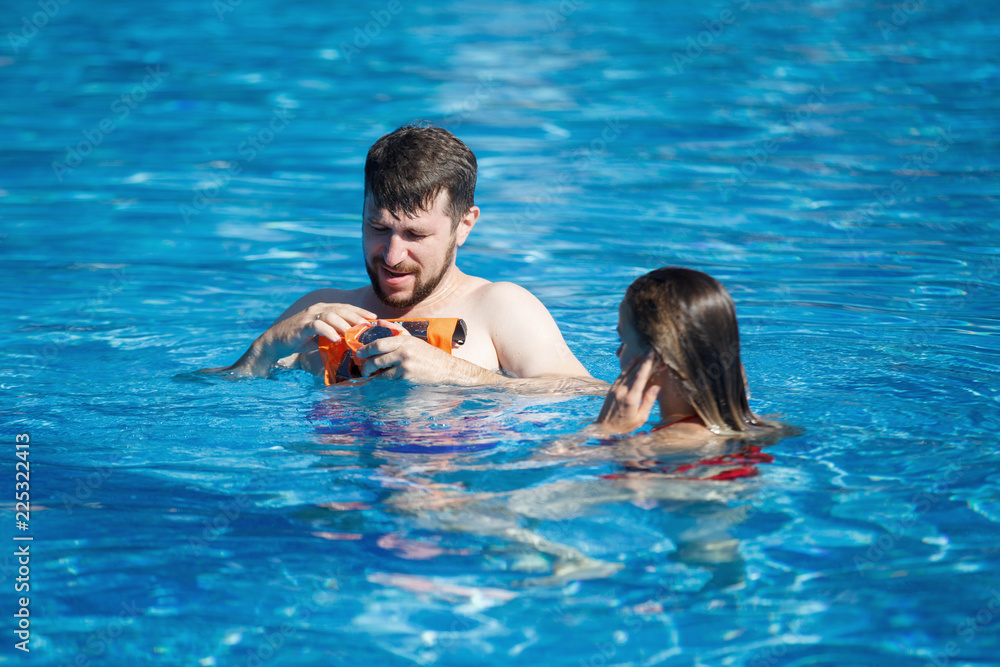 Photographer spends shooting on the camera in the pool. Removes, being in the shoulders in the water. The camera is in a special orange waterproof case.