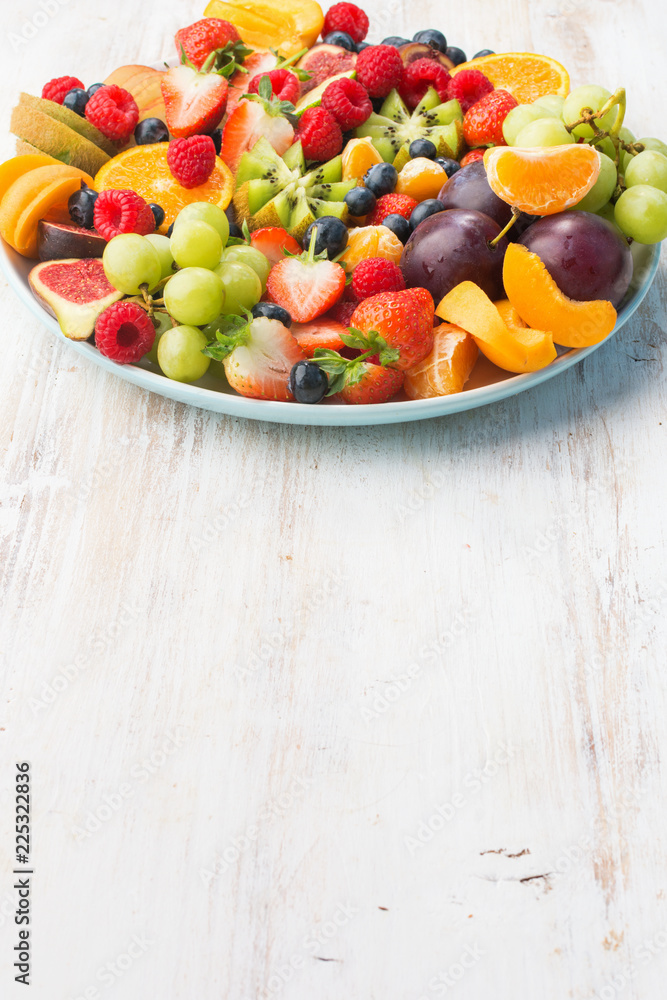 Healthy fruit platter, strawberries raspberries oranges plums apples kiwis grapes blueberries on the white wooden table, vertical, copy space for text, vertical selective focus