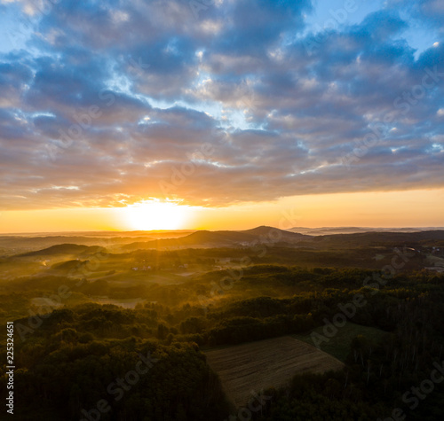 Aerial view of sunrise in foggy morning, forest and field in the foreground, view from air