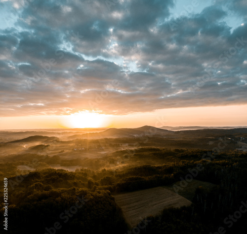 Aerial view of sunrise in foggy morning, forest and field in the foreground, view from air
