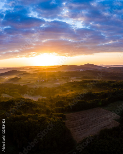 Aerial view of sunrise in foggy morning, forest and field in the foreground, view from air