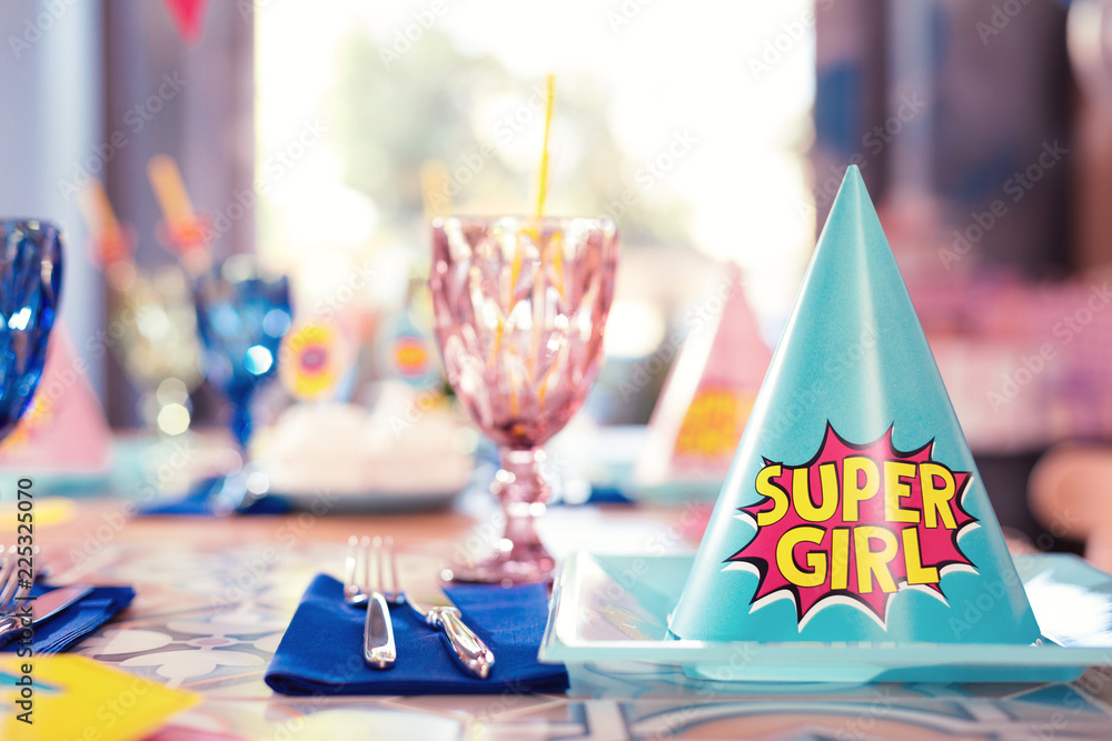 Super girl. Laconic photo of blue party hat fo super girl placed on the plate near the glasses