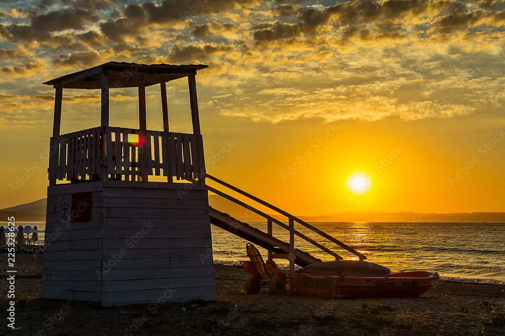 Naklejka premium Early morning, dramatic sunrise over sea and house for rescuers on the beach.