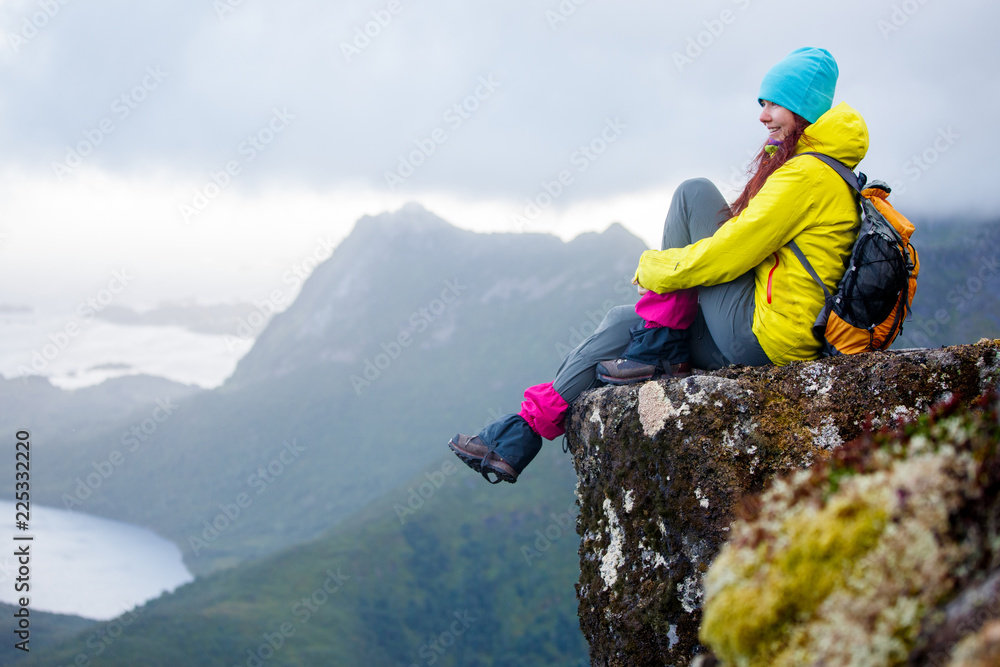 Image of tourist brunette with backpack sitting on top of mountain in background of picturesque landscape
