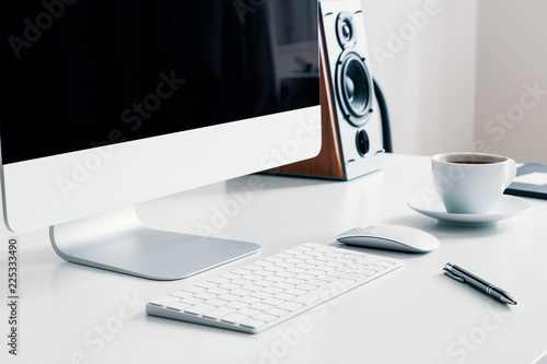 Cup of coffee, keyboard and desktop computer on desk in white home office interior. Real photo photo