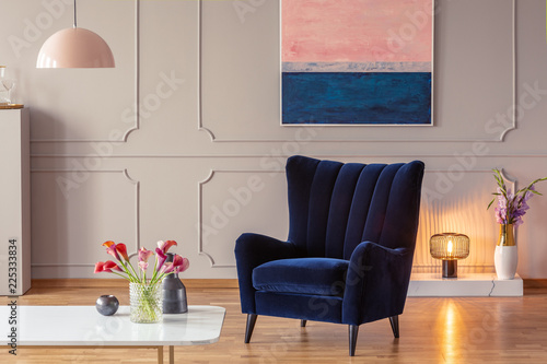 Comfy armchair in a living room interior with a painting, cozy lamp and flowers. Real photo photo