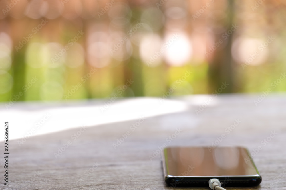 black charging mobile phone on the wooden table on blured nature background. black charging mobile phone on the wooden table on blured nature background.