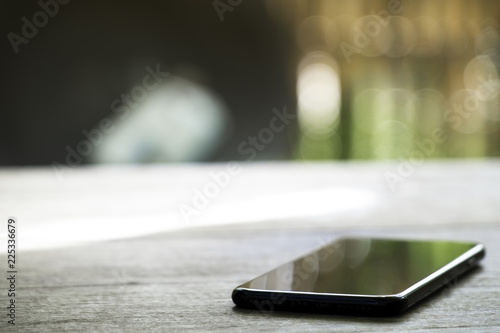 black charging mobile phone on the wooden table on blured nature background.