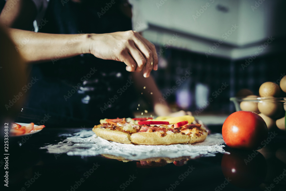 Close up of woman hand putting oregano over tomato and mozzarella on a pizza. Cooking concept