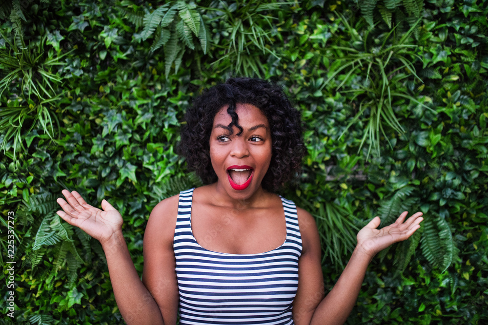 A portrait of a black woman standing against green background of bush leaves. A portrait of a black woman standing against green background of bush leaves.
