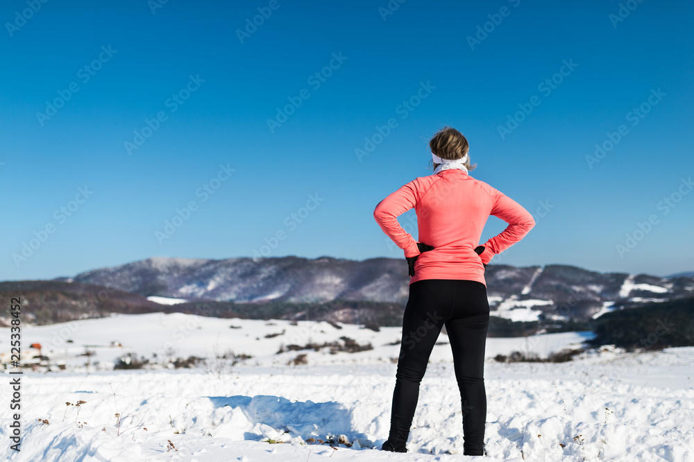 Rear view of senior woman runner resting in winter nature.