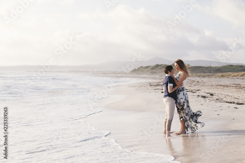Young couple in love hug each other on the deserted beach on a summer evening