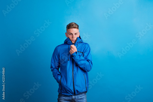 Portrait of a young man with blue anorak in a studio, feeling cold.