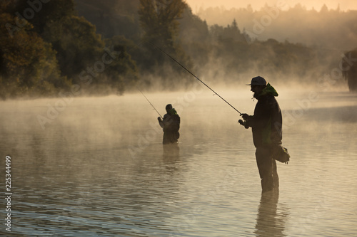 Men fishing in river with fly rod during summer morning.