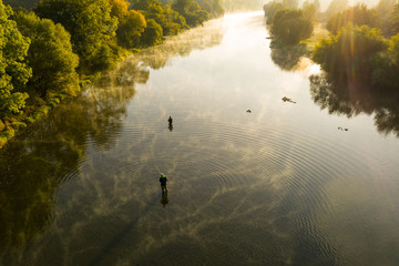 Aerial shot of a man fly fishing in a river during summer morning.