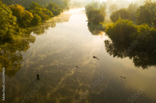 Aerial shot of a man fly fishing in a river during summer morning.