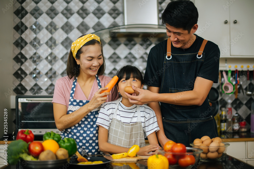 Cute girl help her parents are cutting vegetables and smiling while cooking together in kitchen at home. Cute girl help her parents are cutting vegetables and smiling while cooking together in kitchen at home.