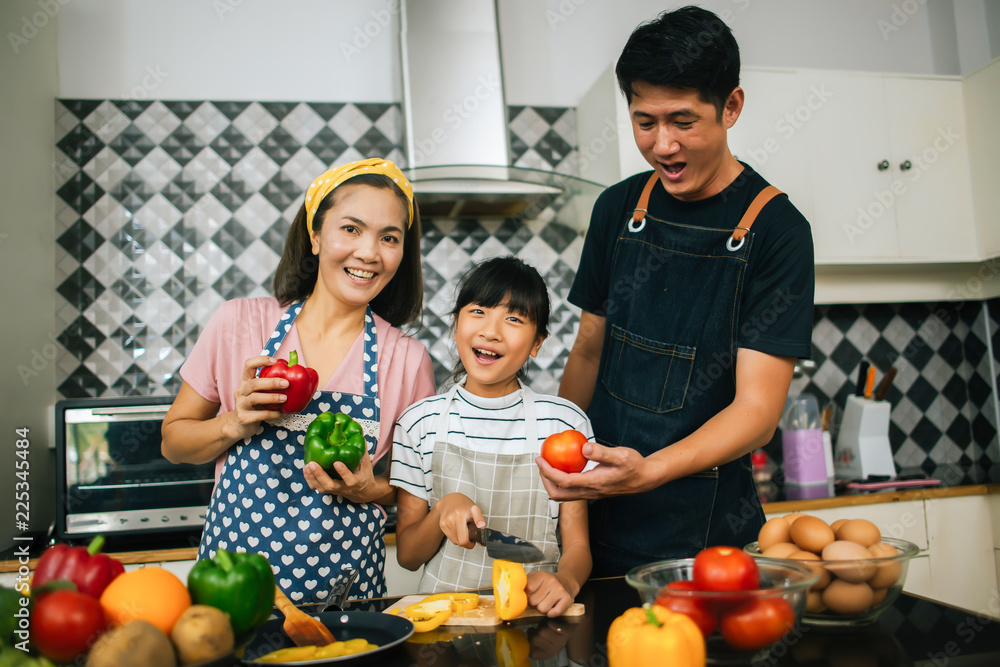 Cute girl help her parents are cutting vegetables and smiling while cooking together in kitchen at home. Cute girl help her parents are cutting vegetables and smiling while cooking together in kitchen at home.