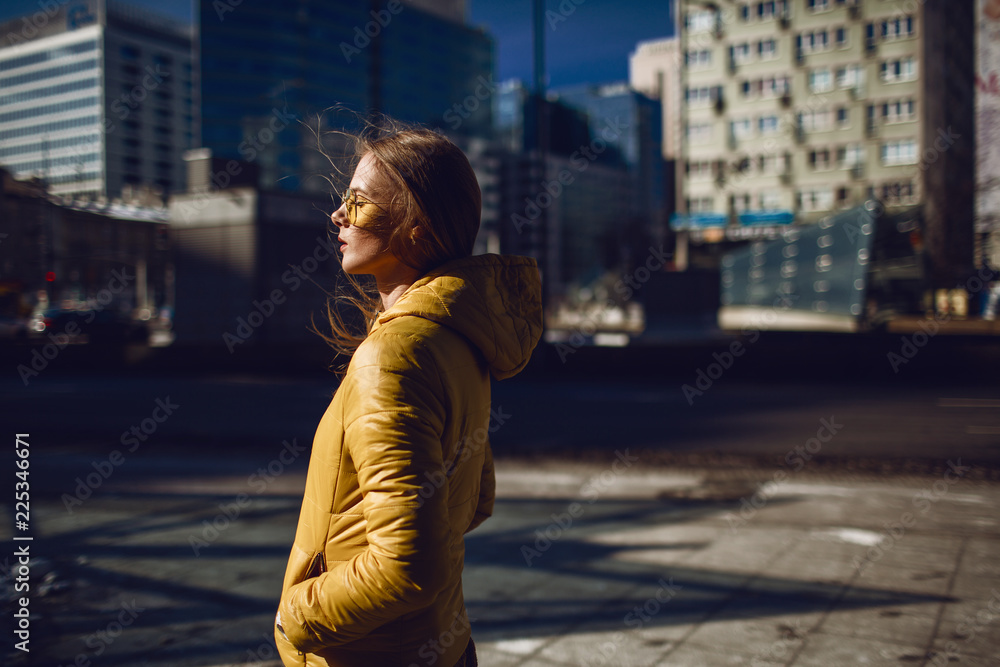 A young European woman, traveling, with long blond hair, wearing a yellow jacket, yellow sunglasses walking down the city center street, street shooting. Even light. A young European woman, traveling, with long blond hair, wearing a yellow jacket, yellow sunglasses walking down the city center street, street shooting. Even light.