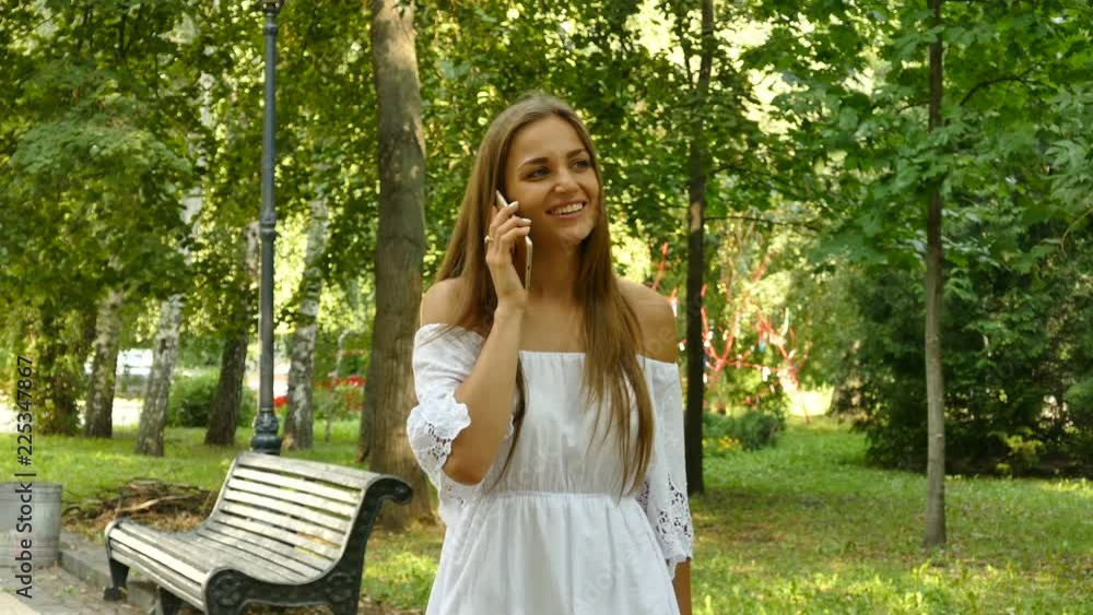   4k. Young  long hair woman  talk mobile smartphone in sunny  city park. 
