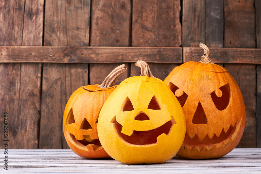 Obraz premium Traditional Halloween pumpkins on wooden background. Funny and scary faces of pumpkins for Halloween holiday. Symbols of Halloween party.