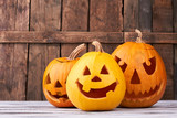 Traditional Halloween pumpkins on wooden background. Funny and scary faces of pumpkins for Halloween holiday. Symbols of Halloween party.