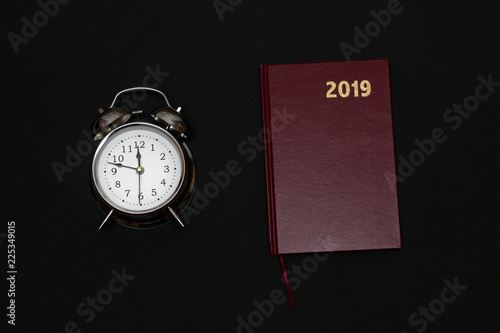 Alarm clock and notebook on black background, 2019 photo