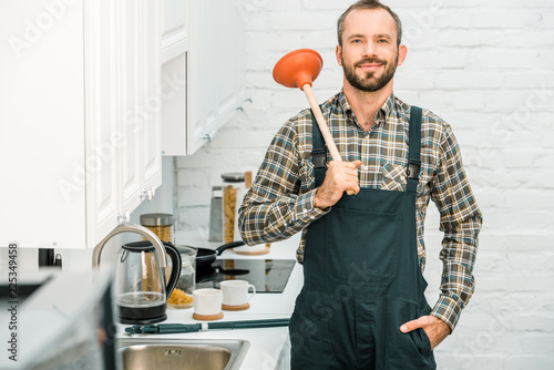Papier peint cheerful handsome plumber holding plunger on shoulder and looking at camera in k