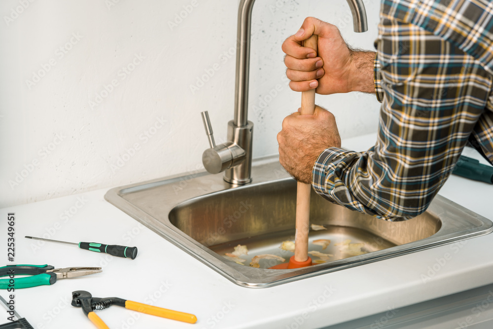 cropped image of plumber using plunger and cleaning sink in kitchen cropped image of plumber using plunger and cleaning sink in kitchen