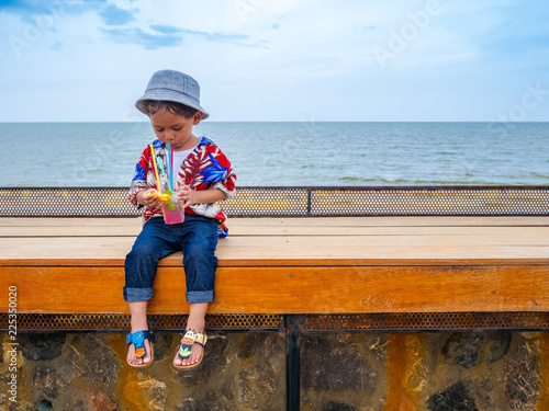 Cute happy asian boy in a summer shirt eating yellow lemon in hand on the wooden table posing background of Hua Hin sea blue skyThailand.Copy-space for your edit. photo