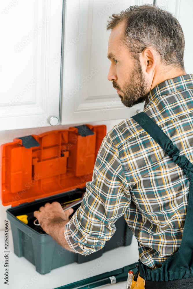 side view of handsome plumber taking tools from toolbox in kitchen side view of handsome plumber taking tools from toolbox in kitchen