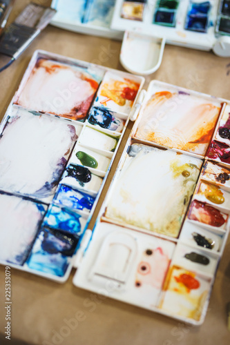 Palette with watercolors in different colors. Various brushes and pencils for drawing prepared by the artist for work.