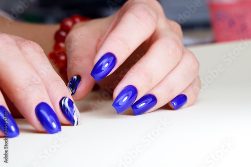 Women s hands are covered with blue gel polish  neat bright manicure. closeup on a bright background.