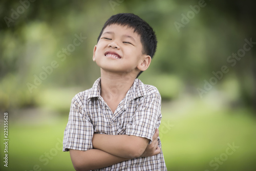 Portrait of cute little boy standing with arms folded and looking at camera with blurred nature background.