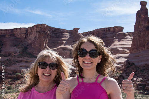 Two female travelers (mother and daughter) give a thumbs up gesture while visiting the beautiful scenery of Arches National Park in Utah photo