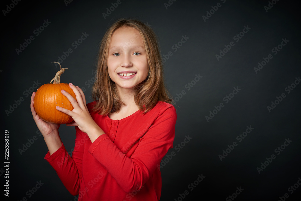 Smiling girl holding ripe pumpkin looking at camera, over dark background Smiling girl holding ripe pumpkin looking at camera, over dark background
