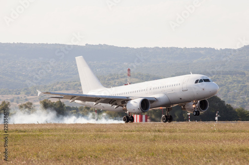 White passenger plane is landing on the airport. Touchdown with tire smoke